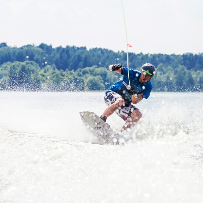 Young active man riding wakeboard on a wave from a motorboat on summer lake